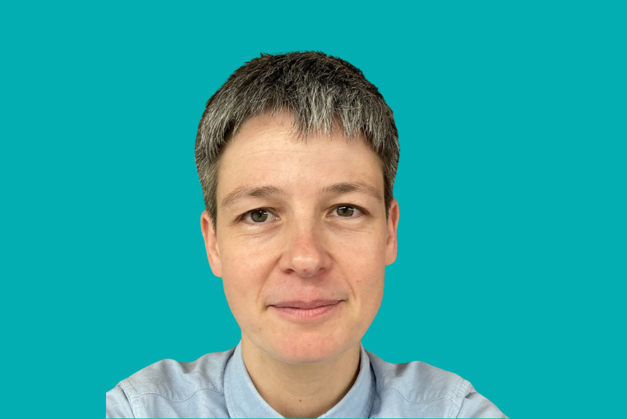 Headshot of a woman with short black hair with grey, she is wearing a light blue shirt.