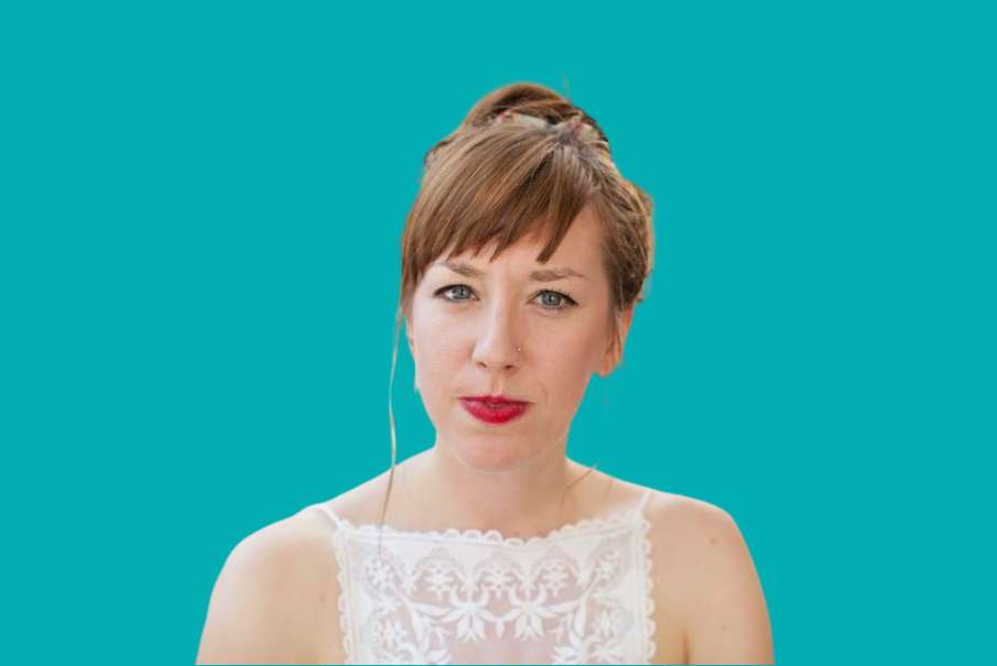 Head and shoulders image of a woman with light brown hair which is in a bun. She is wearing a white top and is smiling. She has a nose piercing.