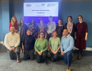 Two rows of smiling people in front of a screen that reads Clinical Education Improvement Fellows Networking Event