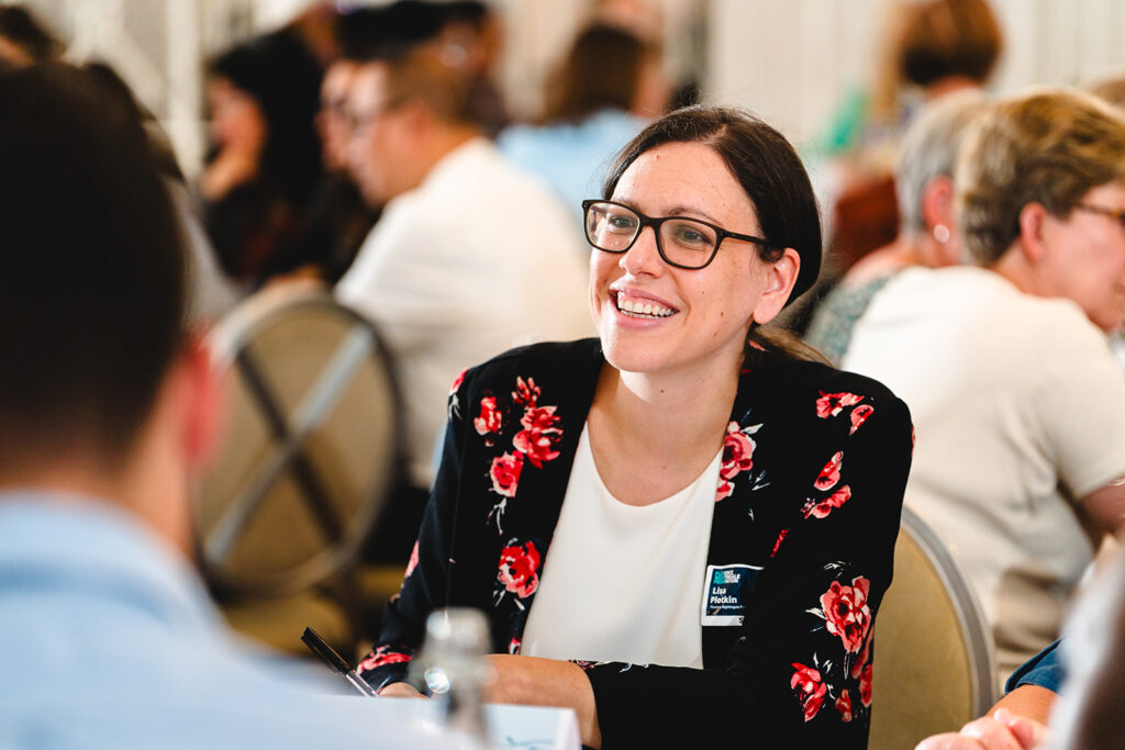 Woman in glasses sitting at a table smiling at others.