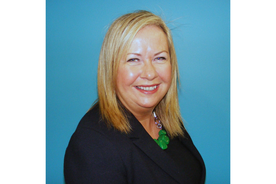 Headshot of a woman with long blonde hair, smiling. She is wearing a dark suit jacket.