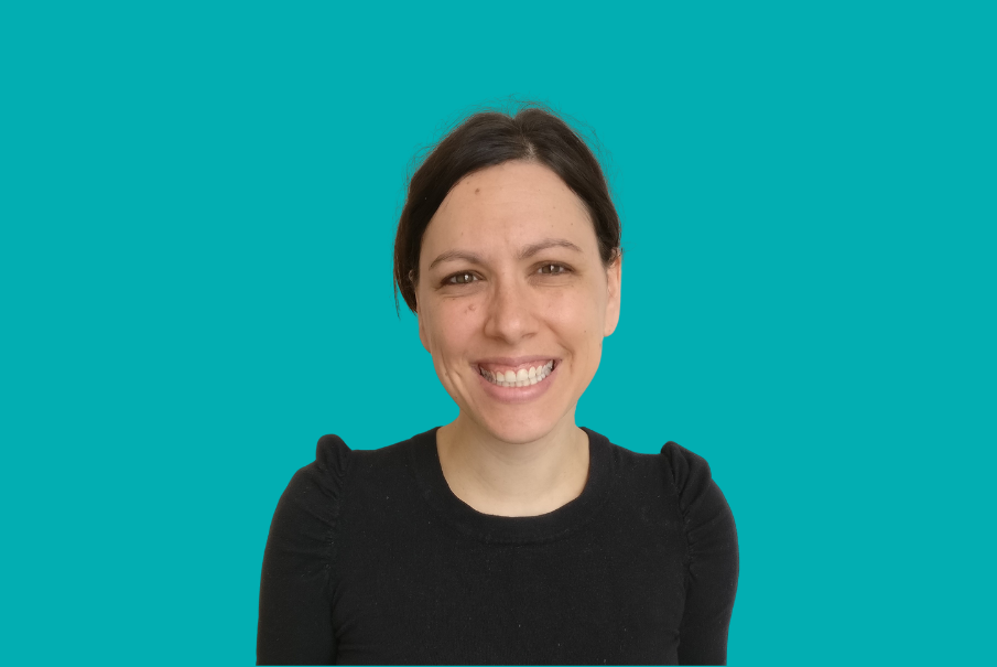 Head and shoulders image of a woman smiling. She has dark brown hair which is tied back and she is wearing a dark coloured top.