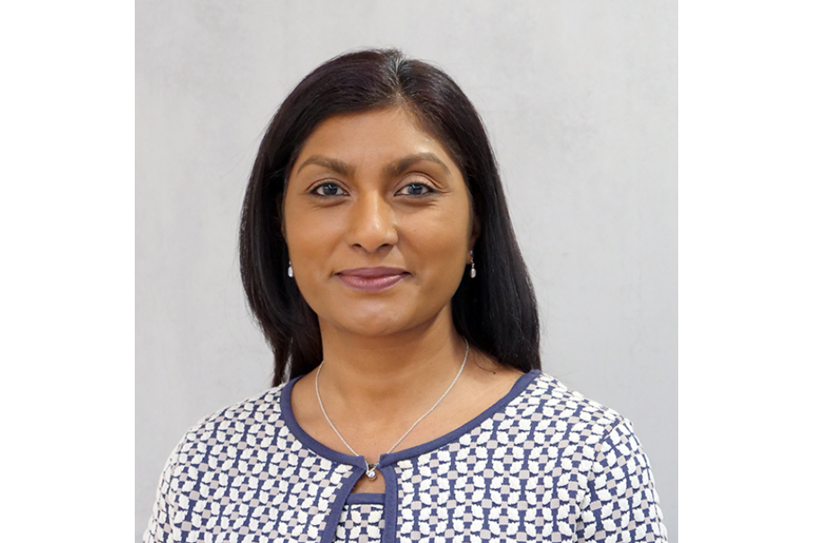 Head and shoulders shot of a woman smiling. She has long dar k hair and is wearing a patterned blue, white and grey jacket and top.