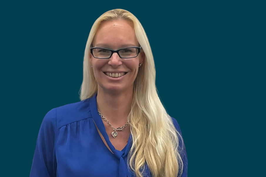 Head and shoulders image of a woman with long blonde hair. She is wearing a mid blue shirt and is also wearing glasses and is smiling.