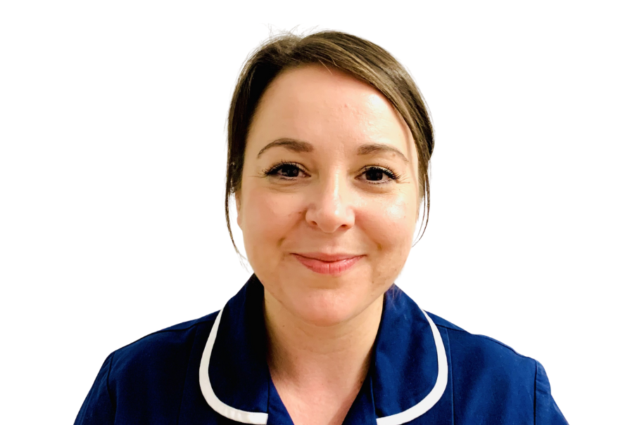 Nurse in a blue uniform with a white trim, this is a head and shoulders image. The nurse has tied back brown hair and she is smiling.