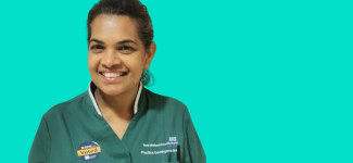 Headshot of a woman in a green NHS uniform, she has black hair tied back and is smiling.