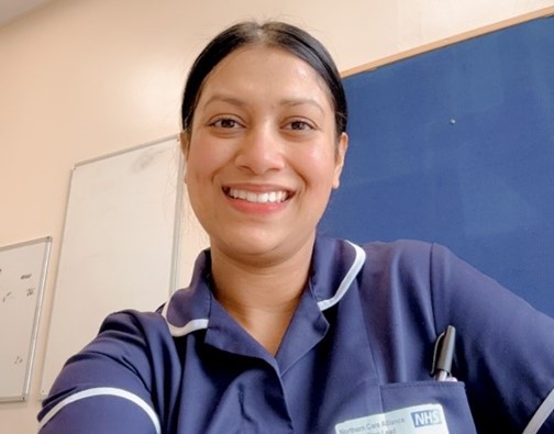 Head and shoulders image of a woman in a dark blue nurses uniform, with dark hair tied back, she is smiling.