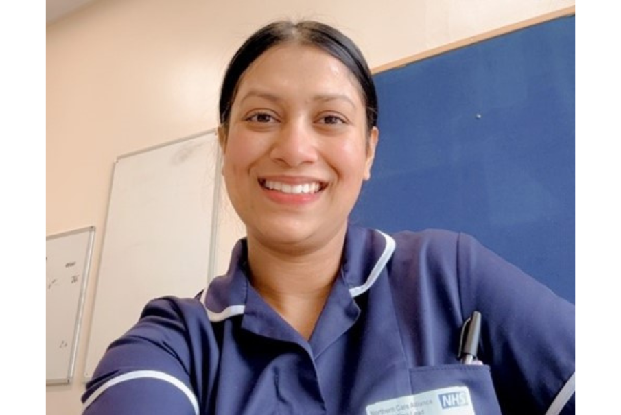 Head and shoulders image of a woman in a dark blue nurses uniform, with dark hair tied back, she is smiling.