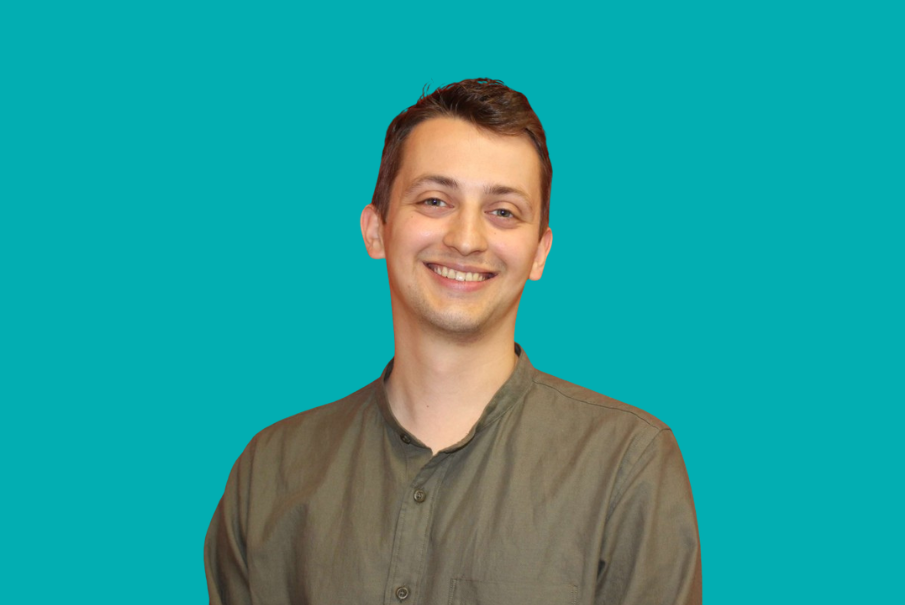 Image of cut out head and shoulders photo of a man with short dark hair wearing a brown shirt and smiling.