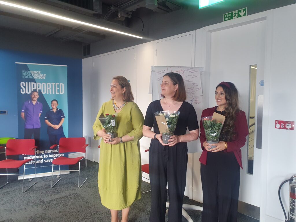 Three woman standing together in a room, with a pull up banner to the left.