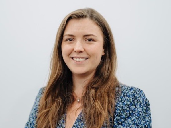 Head and shoulders image of a woman smiling. She is wearing a blue patterned top and has long light brown hair.