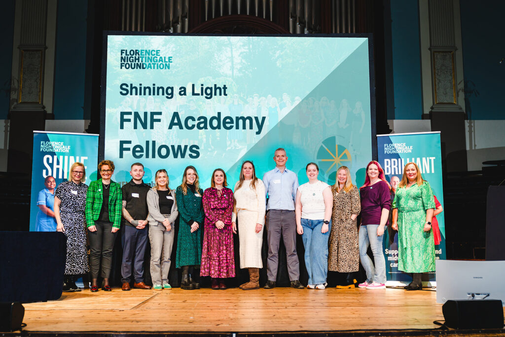 A group of people standing in a line on a stage. They are smiling and standing in front of a large screen which says FNF Academy Fellows.
