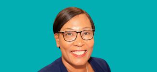 Head and shoulders image of a woman with dark hair, she is wearing a blue top and is also wearing glasses, She is smiling brightly.