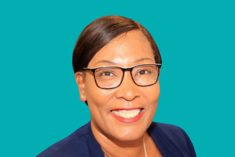 Head and shoulders image of a woman with dark hair, she is wearing a blue top and is also wearing glasses, She is smiling brightly.