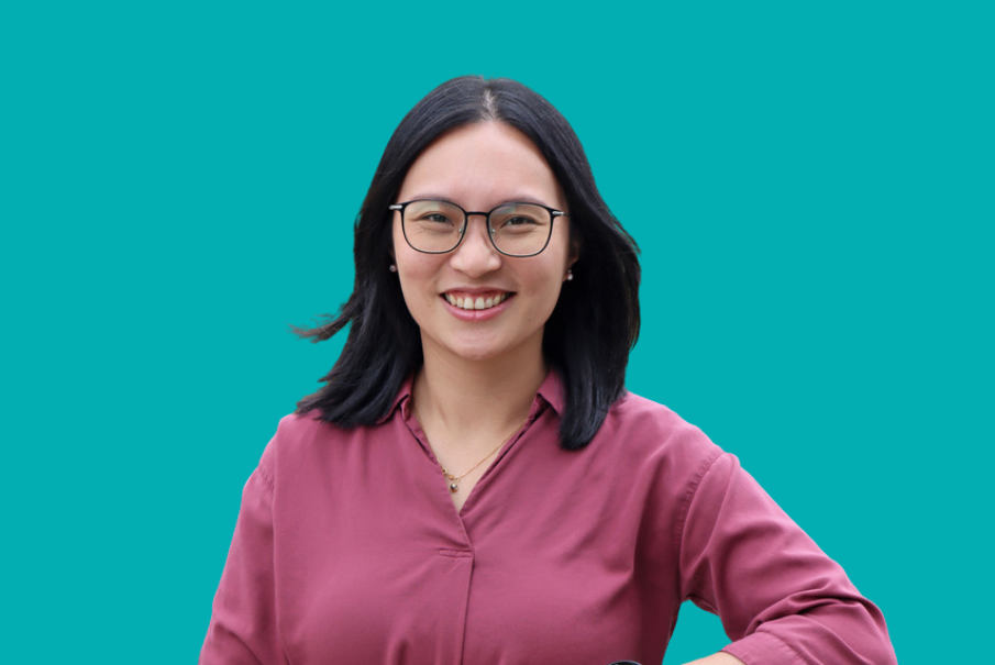 Head and shoulders image of a woman with dark shoulder length hair. She is smiling and wearing glasses. She is wearing a dark pink blouse.