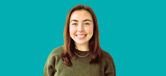Head and shoulders image of a woman with long brown hais she is smiling and wearing an olive coloured jumper.