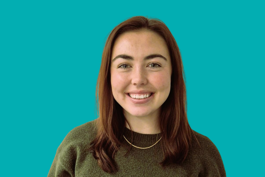Head and shoulders image of a woman with long brown hais she is smiling and wearing an olive coloured jumper.