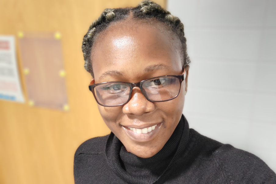 Head and shoulders image of a woman with glasses, wearing a black high neck top, she is smiling brightly.