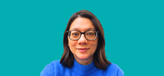 Head and shoulders image of a woman with shoulder length dark hair, she is smiling and wearing dark glasses and a royal blue jumper.