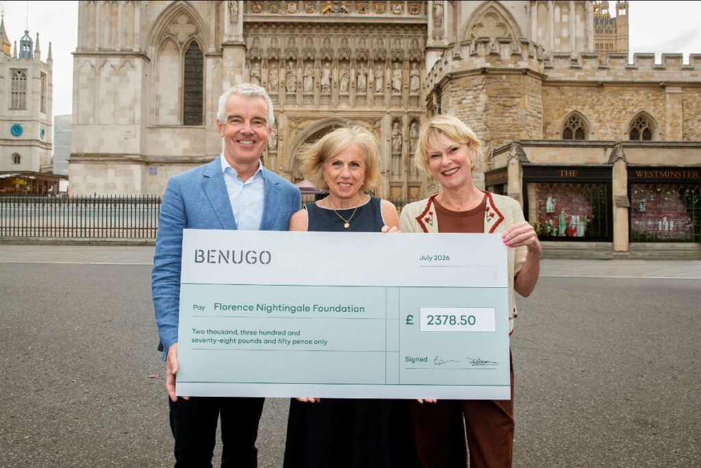 Three people standing outside Westminster Abbey holding a large cheque.