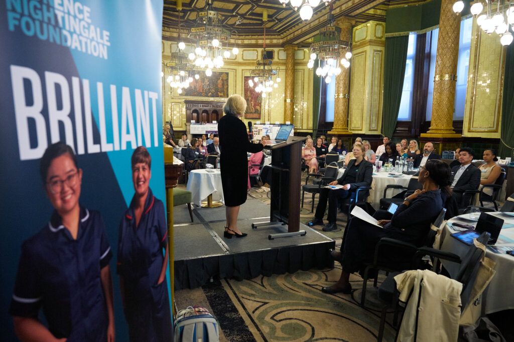 A room full of people sitting at tables listening to someone speaking on a stage.